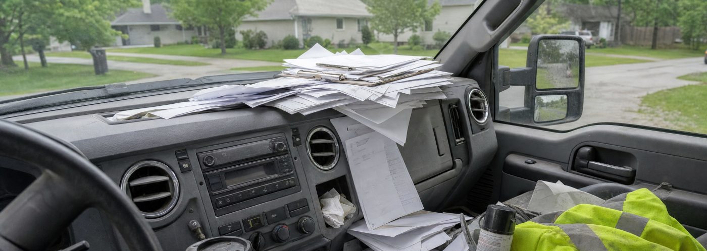 Inside a pickup truck cab: loose locate paperwork piled across the dashboard.